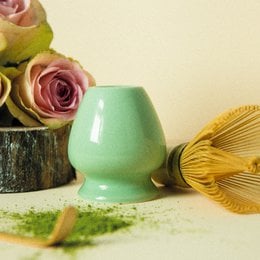Green matcha tea ceremony kit with ceramic whisk holder, bamboo whisk, and wooden spatula for traditional preparation.