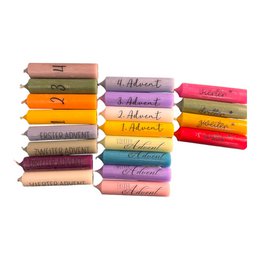 A set of taper candles in various colors, including white, red, and green. The candles are packaged in a gift box with a ribbon and a small teddy bear. The product appears to be a simple gift idea for the holiday season.