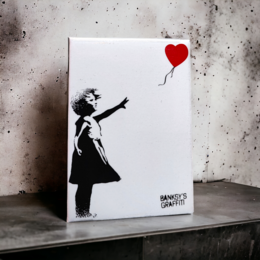  Banksy's Graffiti Fridge Magnet - Girl With Red Balloon. A black and white image of a girl releasing a red heart-shaped balloon, created by the famous street artist Banksy. The magnet is made of a durable material and can be used to display on a refrigerator or other magnetic surface.