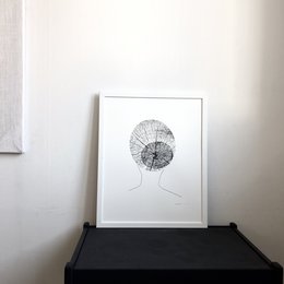 A black and white screen print featuring an abstract, circular design with intricate line work, displayed on a simple white wall.