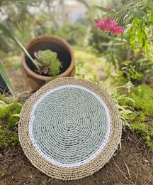 Round woven placemat in aqua and natural colors, made of natural materials, suitable for decorative trays or tabletop use.