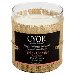 A large, natural peach orchid-scented candle in a glass container with a woven burlap-style label.
