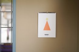 A4 wall calendar with minimalist geometric design featuring a triangle shape and sun icon. Suitable for use as a birthday calendar or general purpose wall calendar.