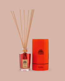  A tall, cylindrical glass reed diffuser with a red liquid and bamboo reeds. The diffuser has a gold-colored cap and base.