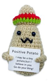  A crocheted toy in the shape of a potato with a positive message. The toy has a round, bulbous shape with a textured surface resembling a potato. It is cream-colored with stripes of red and green around the middle, giving it a playful, whimsical appearance. The toy includes a small tag or label that says "Positive Potato" and conveys an uplifting message.