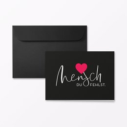 A folding condolence card with a heart design and the text "Mensch du Fehlst" (German for "Human, you are missed") in a handwritten font. The card is available in various color variants including neon orange, glitter red, plain, and glitter silver/pink. The card is A6 landscape size and includes an envelope.