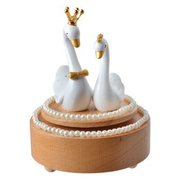  A decorative music box featuring two white swan figurines with gold crowns, sitting on a round orange base. The music box appears to be designed for children or as a decorative piece.