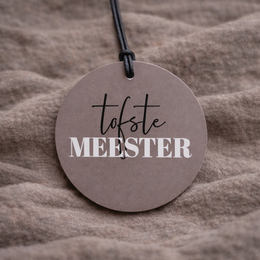  A round, gray keychain with the text "Toffe MEESTER" printed in black. The keychain appears to be made of a durable material and has a black cord attached for easy carrying.