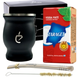 Black ceramic yerba mate gourd with metal rim, bombilla, and yerba mate tea leaves in a box.