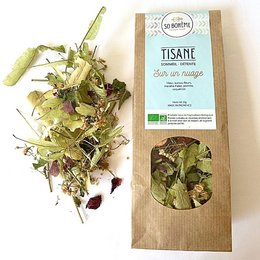Organic herbal tea with a variety of dried leaves, flowers, and herbs. The tea appears to be a blend of different ingredients, including green and purple leaves, small buds, and other natural elements. The packaging indicates it is a "Tisane" or herbal tea.