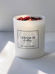 Tall, round white candle with red and purple floral accents, scented with geranium essential oil.