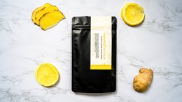 Lemon and ginger flavored matcha tea in a black package, with sliced lemon and ginger root visible around the package.