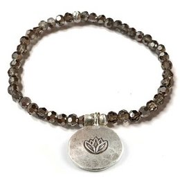 "Lotus bracelet - smoke: A delicate charm bracelet featuring a lotus flower charm and strands of smoky quartz beads. The bracelet has a natural, earthy style that would complement a variety of outfits."
The product is a charm bracelet featuring a lotus flower charm and strands of smoky quartz beads. The bracelet has a natural, earthy style with a neutral color palette of grays and browns. The materials used are likely semi-precious stones or glass beads. The overall shape of the bracelet is delicate and feminine, with the lotus charm adding a symbolic touch.