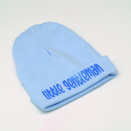 A light blue baby hat with the text "Little Gentleman" printed in blue on the front.