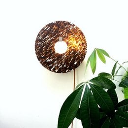 A round, textured wall light with a mix of brown, rose, and mauve colors. The light has a unique, natural-looking design that would complement a variety of decor styles.