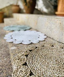 A round, white crocheted placemat with a floral design, placed on a woven straw mat.