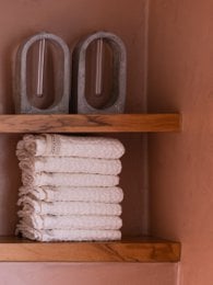 Waffle-textured white and light grey bath towels, available in multiple sizes, neatly stacked on wooden shelves.