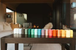 Tall, round candles in various earthy colors including eucalyptus, army green, army brown, and matte black. Displayed on a shelf with abstract ceramic shapes.