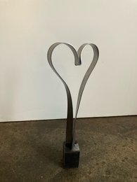 Metal sculpture in the shape of a heart, made of black metal with a curved, abstract design. Suitable for display as a decorative piece or artwork.