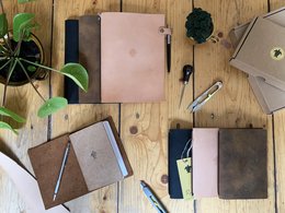 A brown leather-bound notebook with a pen attached, suitable for writing and note-taking.