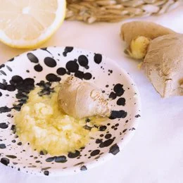 A round, white ceramic plate with a textured, speckled pattern. The plate has a raised edge and is designed to be used as a multifunctional grater for garlic or other small ingredients.