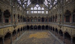 A large, ornate indoor space with intricate architectural details and high ceilings. The space appears to be a historic building or palace, with arched windows, columns, and a grand, open layout.