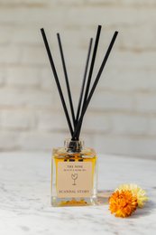 Elegant glass bottle with amber-colored liquid and black reed diffuser sticks. Packaged in a simple brown cardboard box with the brand name "The Noir" printed on it.