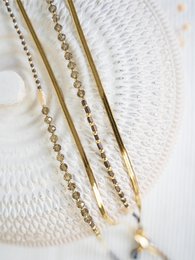 Beige and gold-toned eyeglass cord with a delicate, minimalist design. Features a simple chain-link style and a clasp for attaching to glasses.