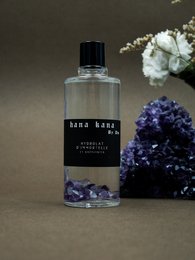 Immortelle hydrosol and amethysts cleansing product in 50ml and 100ml sizes, featuring a glass bottle with a black label and purple amethyst crystals.