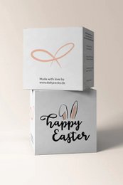 A white gift cube with the text "HAPPY EASTER" printed on it. The cube is decorated with a simple ribbon-like design in a light color.