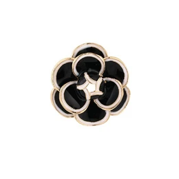 Black flower brooch with gold-tone metal petals and circular design, elegant statement piece.