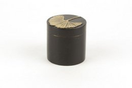 A round, black pill box with a ginkgo leaf pattern on the lid, made of stone material. Suitable for storing small items or medications.