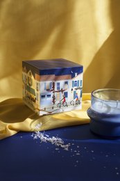 Tall, round, white scented candle in a blue and white patterned box.