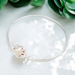 Elegant silver-plated bangle bracelet with minimalist dandelion seed charm. Delicate and feminine jewelry piece.