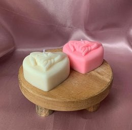 Heart-shaped candles in various pastel colors, including white, pink, and yellow. The candles are displayed on a wooden stand, creating a romantic and soothing atmosphere.
