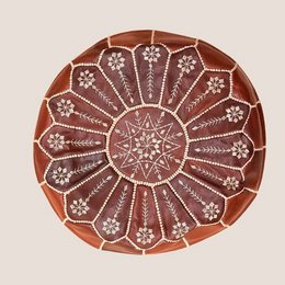 Pouf KALA is a round, decorative ottoman with a geometric, star-shaped pattern in shades of brown and white. The intricate design features a central star surrounded by radiating lines and shapes, creating a visually striking and textured surface.