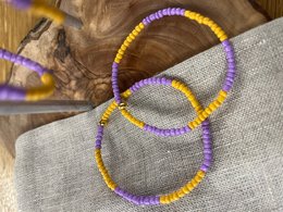  "Glass bead bracelet in purple and orange colors, featuring a beaded design with a circular shape."
