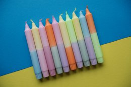 Pastel-colored dinner candles in a variety of soft, muted shades including pink, yellow, green, and blue.