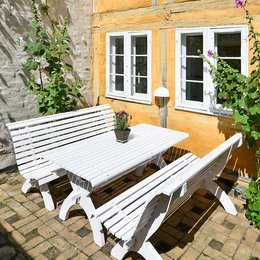 A white wooden garden set with a bench and table, suitable for outdoor seating and dining. The set has a simple, minimalist Nordic design that would complement a variety of garden styles.