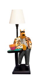  A tall, black desk lamp with a white lampshade. The base of the lamp features a carved wooden figure of a wolf or similar animal, with colorful accents and details.