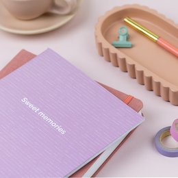 A5 lined notebook in a soft lilac color with a simple, minimalist design. Features a small decorative icon on the cover.