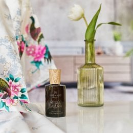 Home fragrance spray with floral and botanical design, featuring a glass bottle with a green color and a wooden cap.