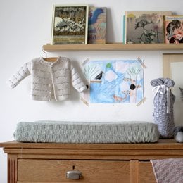 Mint green knitted cotton changing pad cover for small spaces in a child's room. Features a soft, textured surface and neutral color to complement various decor styles.
