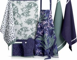  This apron features a floral and leaf print design in shades of green and purple. The material appears to be a durable, textured fabric suitable for kitchen or gardening use. The apron has a bib-style top and ties at the waist for a secure fit.
