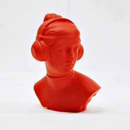 Vibrant red statue of a female figure with an abstract, futuristic style. The statue has a rounded, minimalist shape and appears to be made of a glossy, synthetic material.