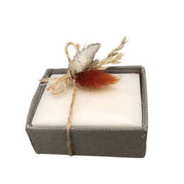  A gray linen box containing a bar of soap, decorated with a feather and twine.