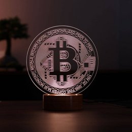 A wooden table lamp with a Bitcoin symbol illuminated on the base. The lamp has a dark, minimalist design.