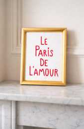 Framed poster with text "Le Paris de l'amour" in a gold frame, accompanied by a white ceramic mug with the same text.