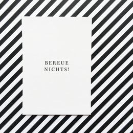 Postcard with the German text "Bereue nichts!" which translates to "Don't regret anything!" The postcard has a minimalist, typographic design with the text centered on a plain white background.