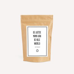 Colorful gummy candies in a brown paper bag with the text "The sweetest mom in the whole world | TOOT Candy bag". The bag is accompanied by a small figurine of an owl and a tin can.